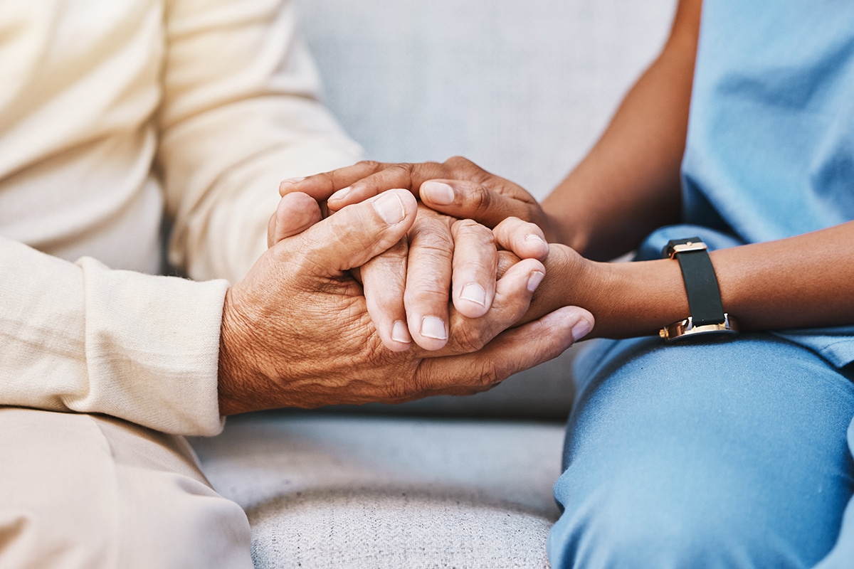 Nurse and senior patient holding hands for comfort
