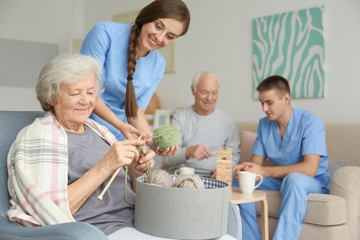 Senior woman knitting with assistance of her caregiver at home