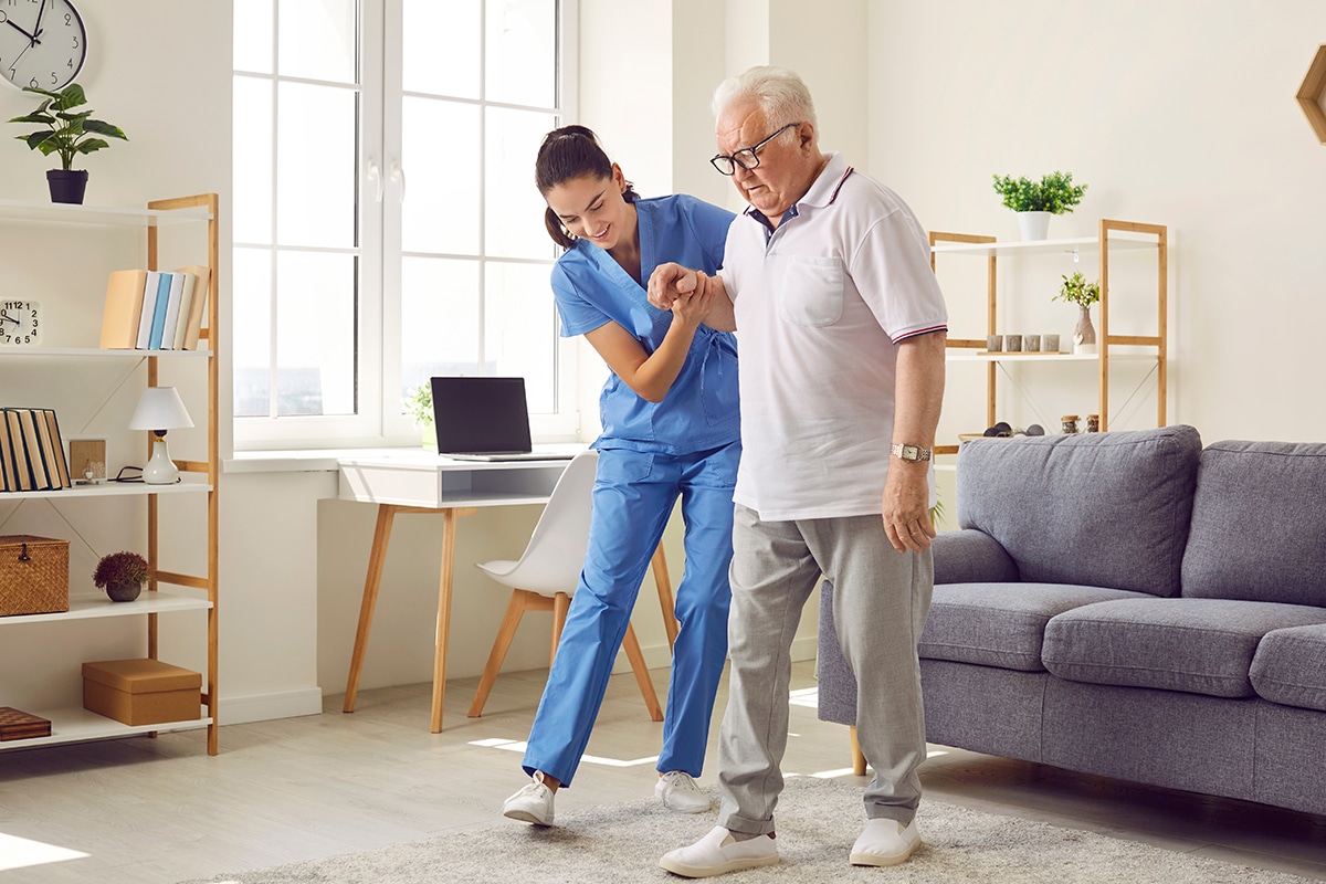 Nurse in assisted living facility holding elderly patient by hand and helping him walk